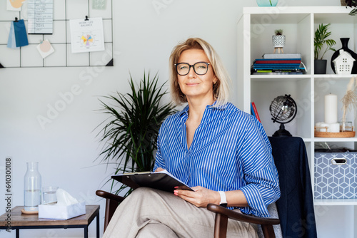 Professional Psychotherapy. Successful female Psychologist Smiling To Camera Sitting On armchair In Office. Mature 50s middle-age professional portrait of teacher, coach, mentor, therapist, counselor photo