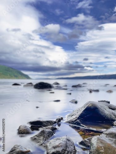 Loch Ness and cloudy blue sky. Selective focus on the rocks on foreground.