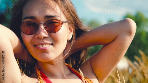 Happy free asian woman walking in tall grass on a sunny summer day. Portrait of a hippie woman in a bright orange boho style top photo