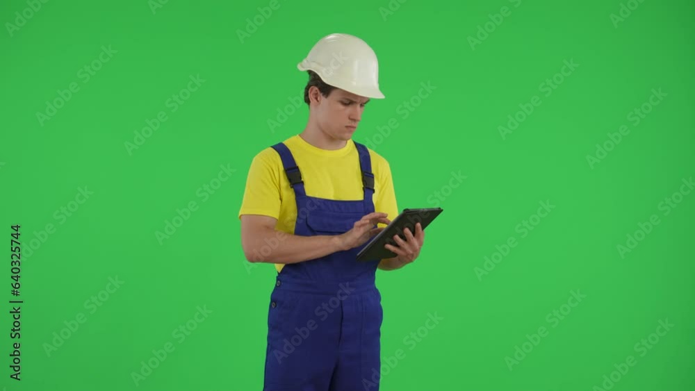 Medium green screen isolated chroma key video of a young construction worker holding a tablet and typing, inserting data while looking around. Medium green screen isolated chroma key video of a young construction worker holding a tablet and typing, inserting data while looking around.