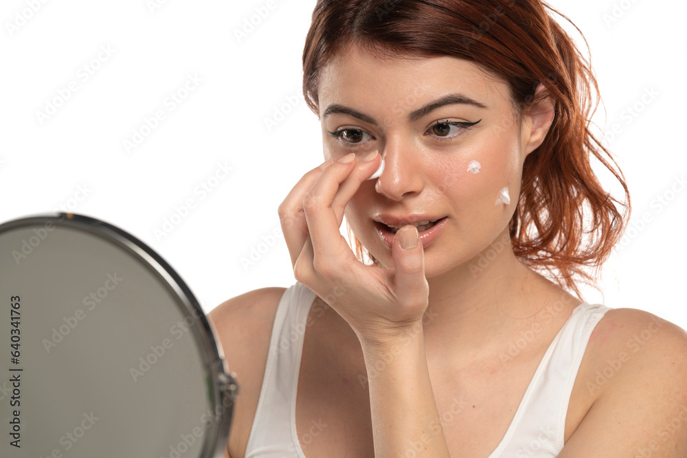 Beauty portrait image of pretty redhead smiling woman applying face cream isolated over white background Beauty portrait image of pretty redhead smiling woman applying face cream isolated over white background