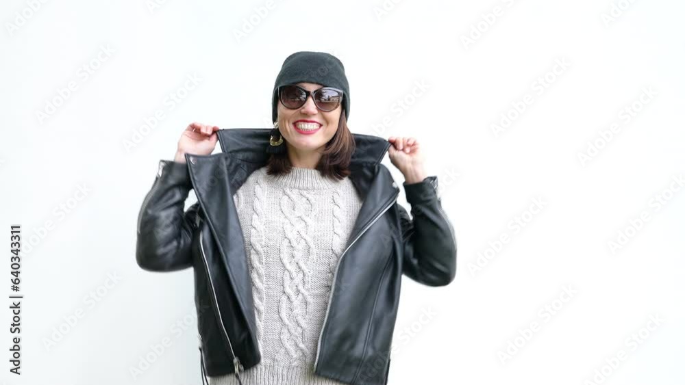 Beautiful female cheerfully smiling and posing in front of white wall dressed in knitted sweater, black leather jacket and Beanie hat 4K footage Beautiful female cheerfully smiling and posing in front of white wall dressed in knitted sweater, black leather jacket and Beanie hat 4K footage