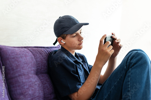 Teenager boy relax sit on sofa at home using cellphone - texting chatting with friend  listening music with earphones and mobile phone  shop online or check mobile application or social media
