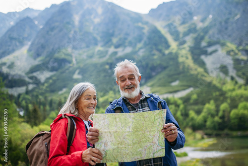 Senior tourists with backpacks reading map, preparing for hike.