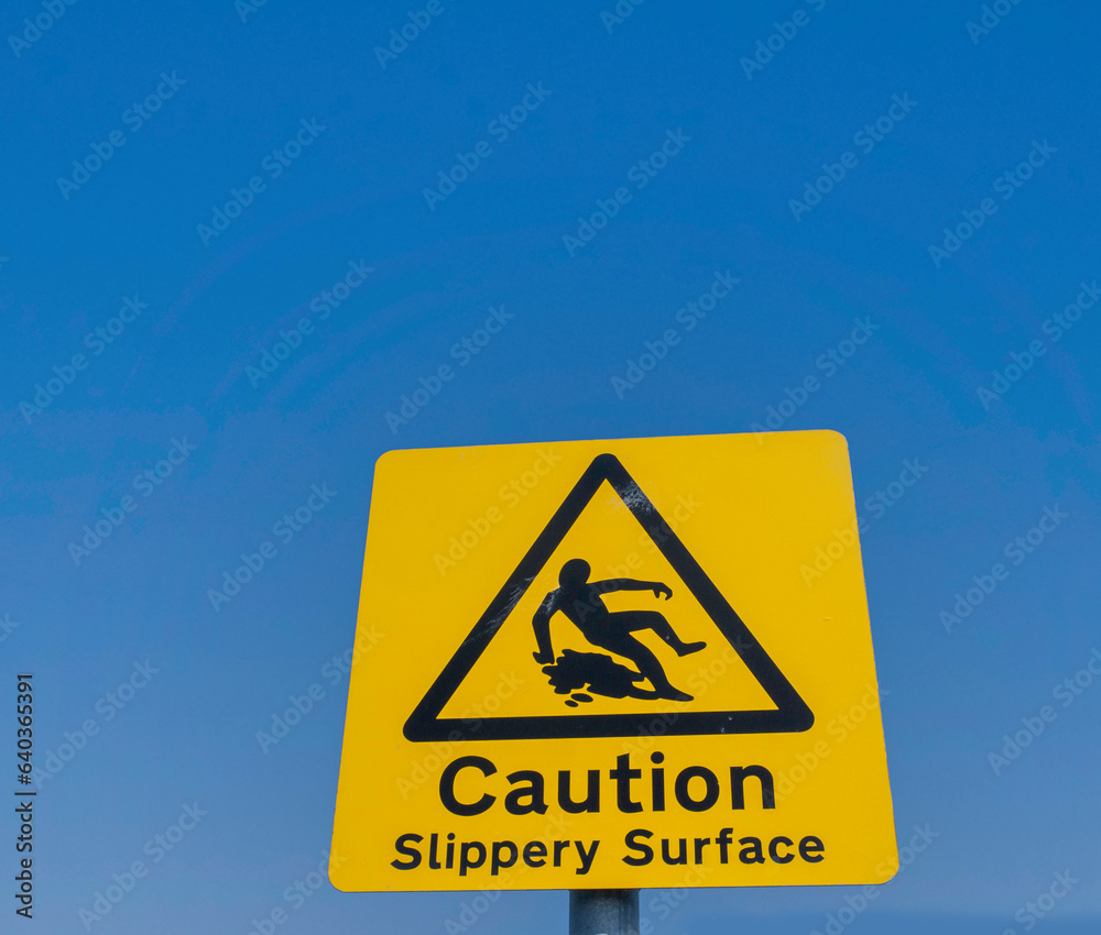 Signage for a slippery surface, a yellow sign set agains a clear blue sky. Signage for a slippery surface, a yellow sign set agains a clear blue sky.