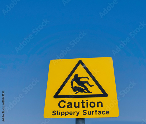 Signage for a slippery surface, a yellow sign set agains a clear blue sky.