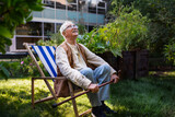 Portrait of smiling senior man resting after taking care vegetable plants in urban garden.