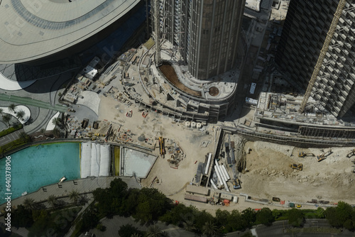 Heavy machinery is busy at work in a sandy clearing at a construction site, where a new high-rise is being completed. The scene is typical of Dubai where major development projects are found citywide.
