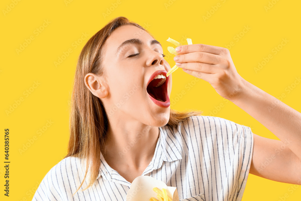 Beautiful young woman eating french fries on yellow background Beautiful young woman eating french fries on yellow background