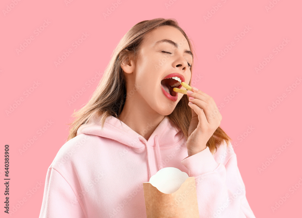 Beautiful happy young woman eating french fries on pink background