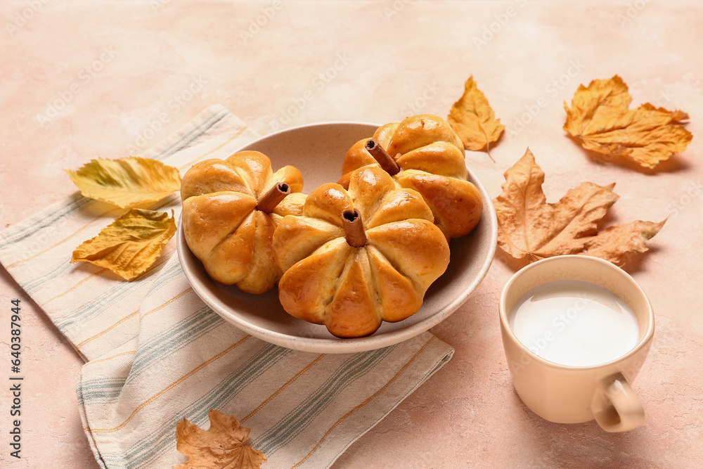 Bowl with tasty pumpkin shaped buns and cup of milk on beige background