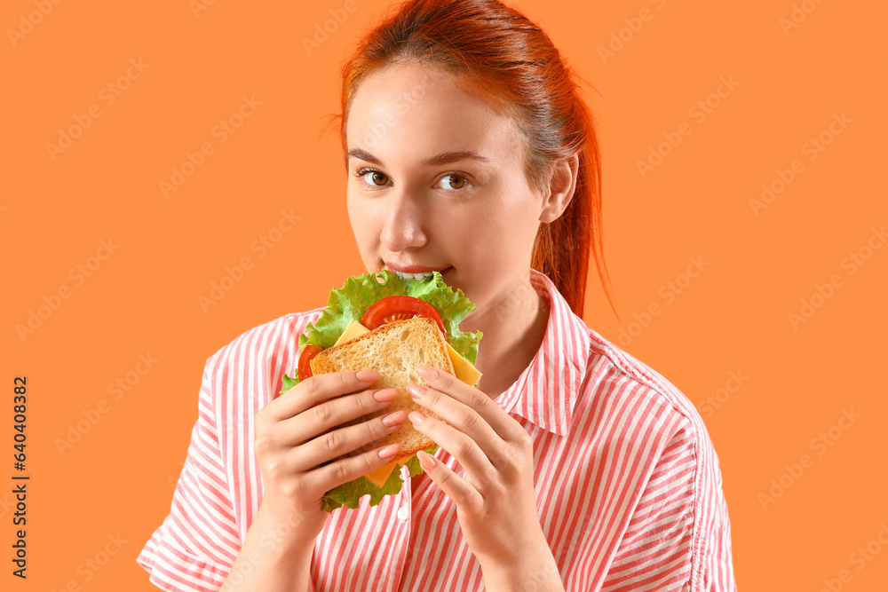 Young redhead woman eating tasty sandwich on orange background, closeup Young redhead woman eating tasty sandwich on orange background, closeup
