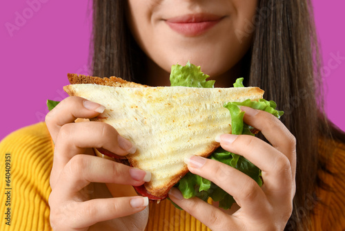 Young woman with tasty sandwich on purple background  closeup