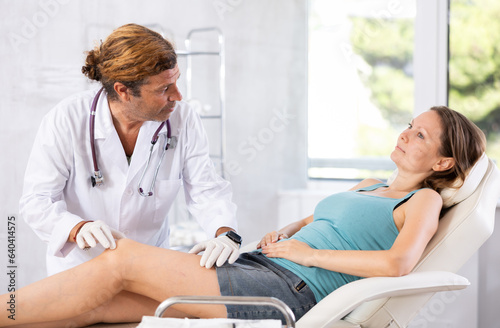 Attentive doctor man examining the sore knee of a female patient