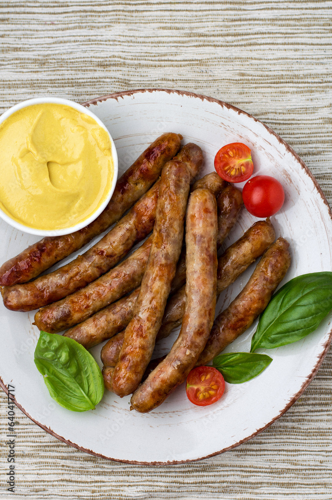 Grilled sausages on a plate with cherry tomatoes, basil and mustard, top view. Grilled sausages on a plate with cherry tomatoes, basil and mustard, top view.