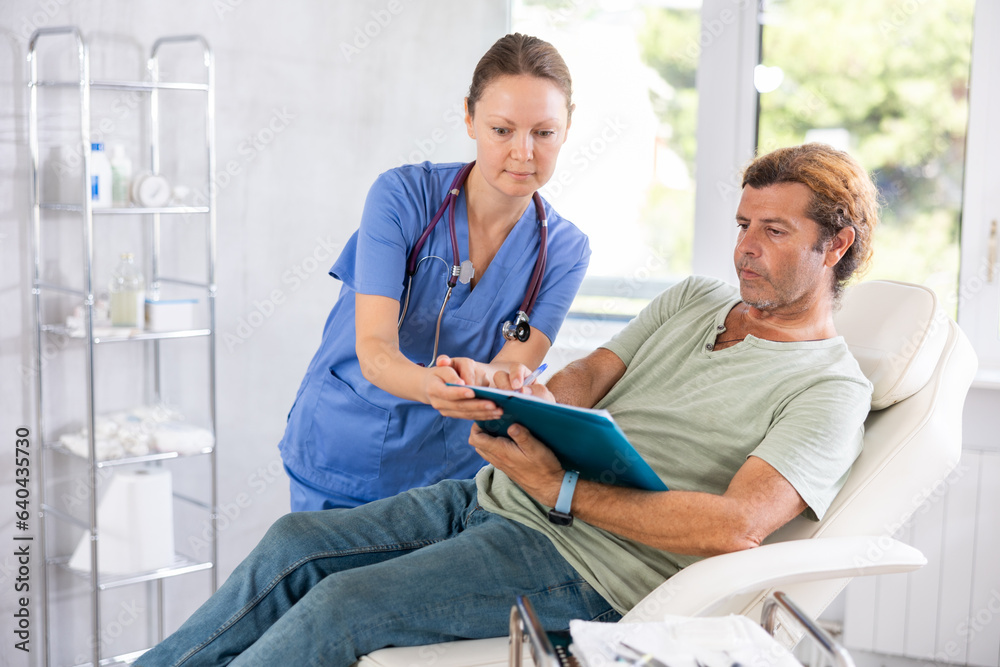 Obraz premium Adult female doctor in medical uniform signing contract with adult male patient in medical room