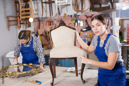 Cheerful young female furniture restorer showing his vintage furniture workshop © JackF