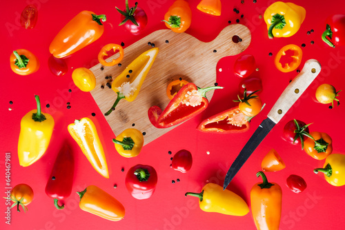 peppers and red tomatoes cherry on a cutting board. Knife and slices of fresh vegetables. levitation on a red background. View from above