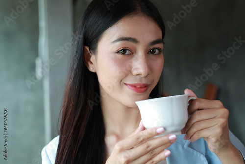 Portrait of smiling happy cheerful beautiful pretty Asian woman drinking coffee or tea in a cafe.