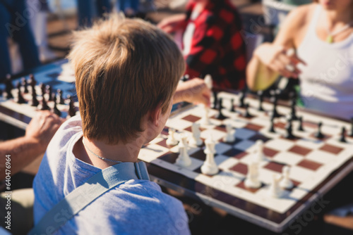 Chess tournament, kids and adults participate in chess match game outdoors in a summer sunny day, players of all ages play, competition in chess school club with chessboards on a table photo