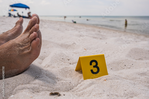 One yellow crime scene evidence marker next to the foot of a corpse laying on the beach after a murder shooting stabbing body forensics csi