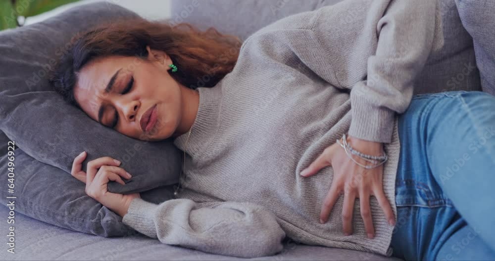 Person, sick and period pain on home sofa with endometriosis, colon crisis and ibs constipation. Biracial woman, stomach ache or stress from tummy virus, gut health risk and gastrointestinal bloating