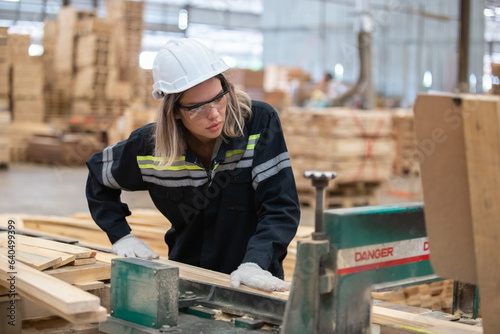 woman engineer carpenter wearing safety uniform and hard hat working on wood cutting electric machines at workshop manufacturing wooden. Female carpenter worker wood warehouse industry.