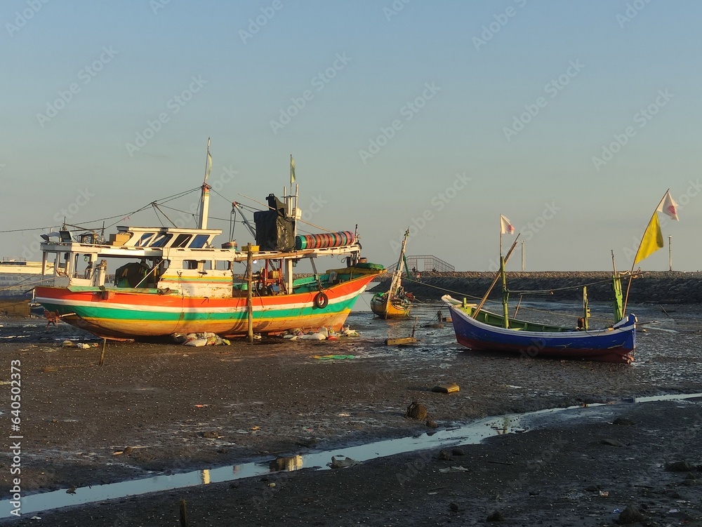 a wooden fishing boat stranded on a beach where the sea water recedes, so they are waiting for the tide to go out to sea to find fish