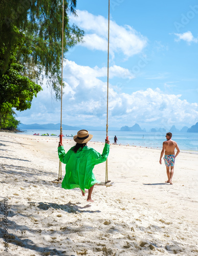 a couple of men and women are on the beach of the tropical Island Naka Island near Phuket Thailand, the woman is at a swing on the beach. Naka Island Phuket Thailand
