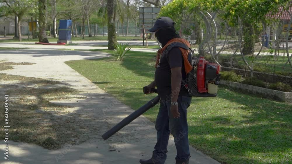 A gardener using a leaf blower to clear up leaves in a garden. A gardener using a leaf blower to clear up leaves in a garden.