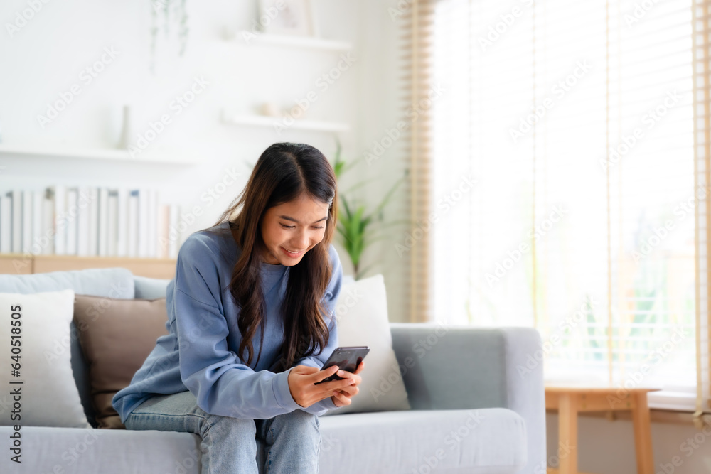 Happy young asian woman relax on comfortable couch at home texting messaging on smartphone, smiling girl use cellphone, chatting online message, shopping online from home Happy young asian woman relax on comfortable couch at home texting messaging on smartphone, smiling girl use cellphone, chatting online message, shopping online from home