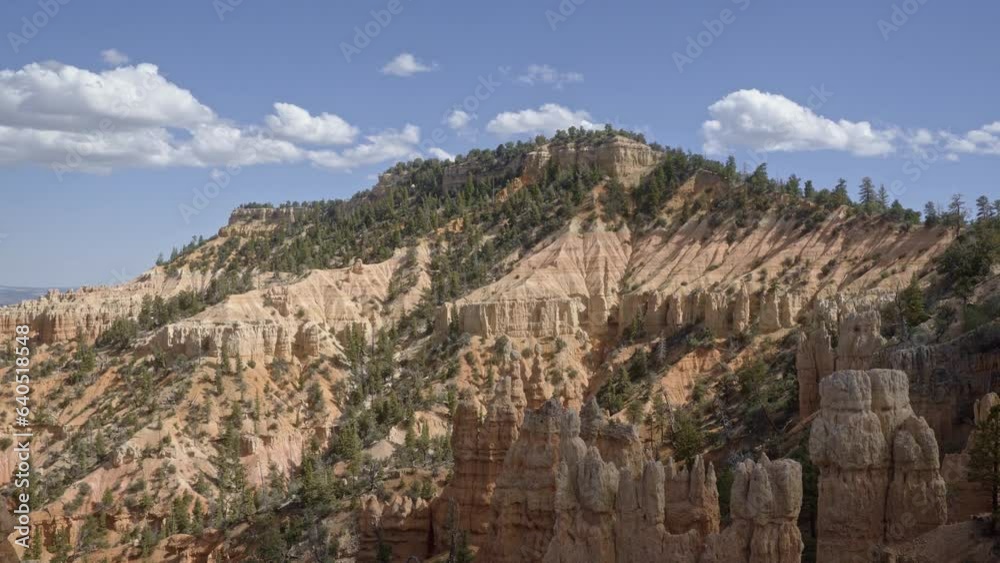 Tilt up shot revealing a large orange sandstone mountain surrounded by hoodoo formations and pine trees in the desert of Southern Utah on a warm sunny summer day Tilt up shot revealing a large orange sandstone mountain surrounded by hoodoo formations and pine trees in the desert of Southern Utah on a warm sunny summer day