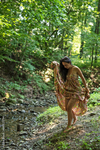 Woman walking barefoot in long dress in a forest among green. Relax with nature and happy summer. Vertical.