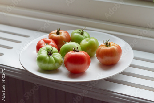 Red and green tomatoes on a plate let to ripen on a window sill in the light from a window.