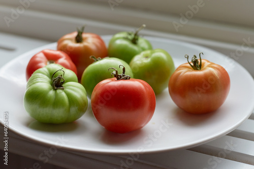 Red and green tomatoes on a plate let to ripen on a window sill in the light from a window.