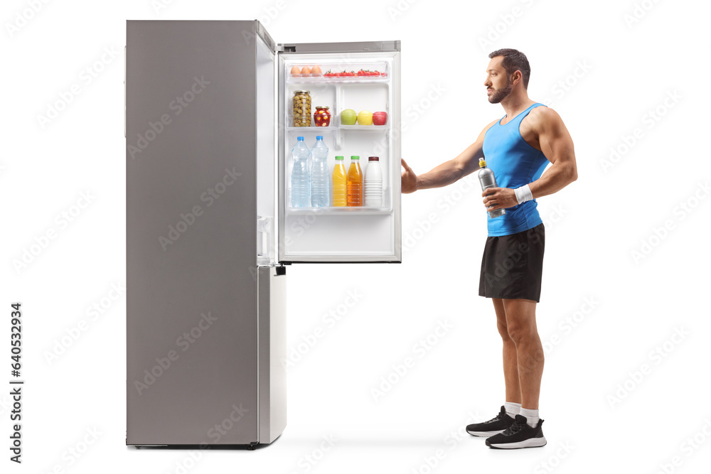 Male athlete holding a sports drink and opening a fridge Male athlete holding a sports drink and opening a fridge