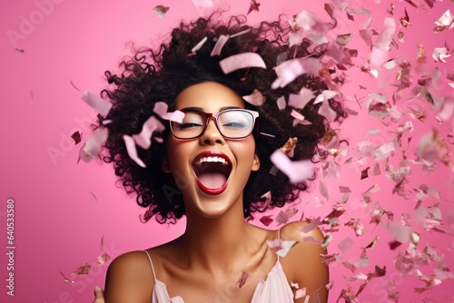 Fun party girl, smiling woman throwing confetti on a pastel pink background. Composition for birthday or woman's day. Party time concept.