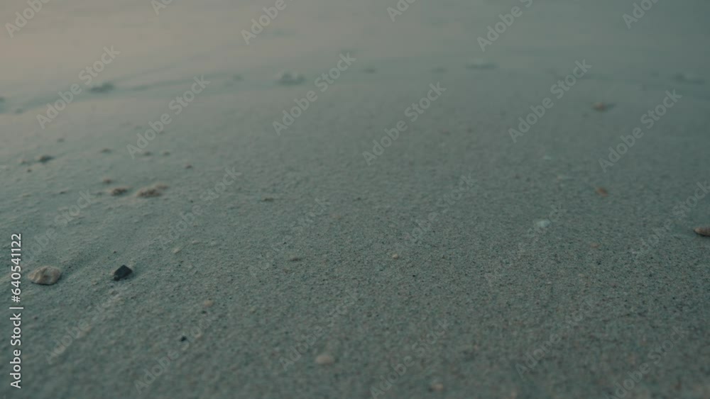 Slow slider shot of people walking barefoot on a peaceful beach with calm waves sweeping the shore Slow slider shot of people walking barefoot on a peaceful beach with calm waves sweeping the shore