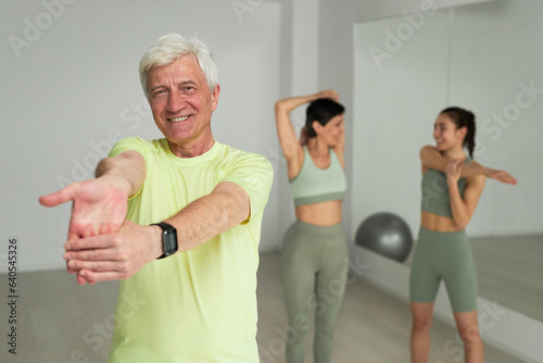 Portrait of senior man smiling at camera while exercising together with people in studio