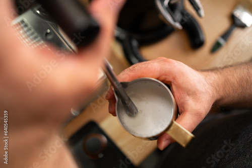 Male barista froths milk on a coffee machine for making cappuccino or latte. Concept of making drinks from natural coffee. Close-up.