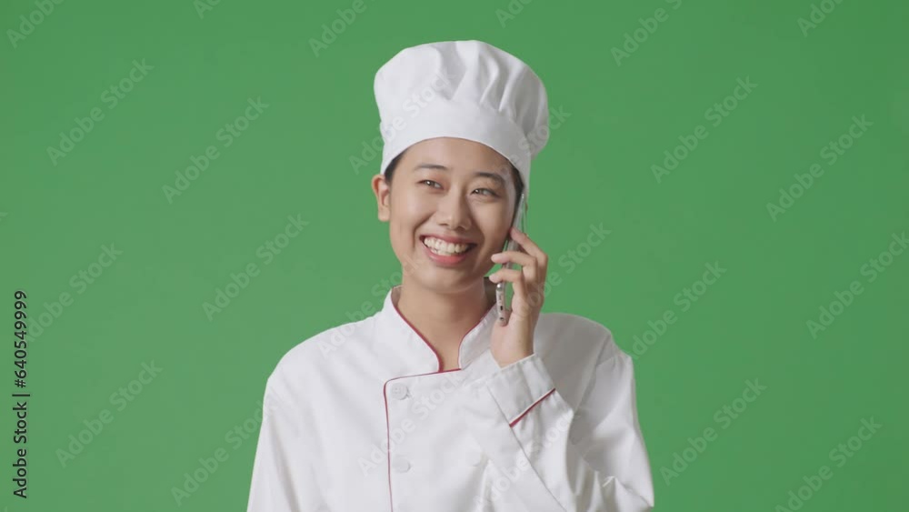 Asian Woman Chef Talking On Smartphone While Walking In The Green Screen Background Studio
