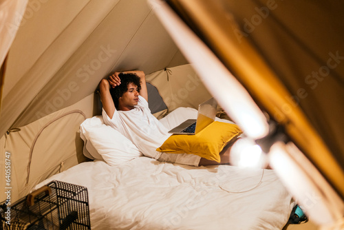 latin man watching a series on the computer lying on the bed in a tent