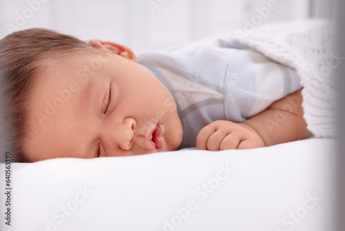 Cute newborn baby sleeping under white plaid on bed, closeup