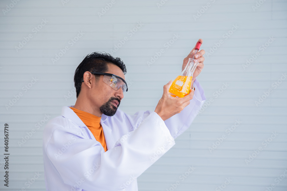 Hispanic or Indian scientist professor wearing lab coat and safety protection glasses looking to liquid experiment in flask glass in laboratory room, specialist or science teacher prepare teaching