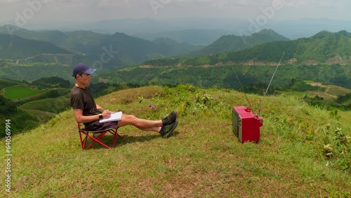 young man watches television in a relaxing outdoor atmosphere, taking notes on an important broadcast photo