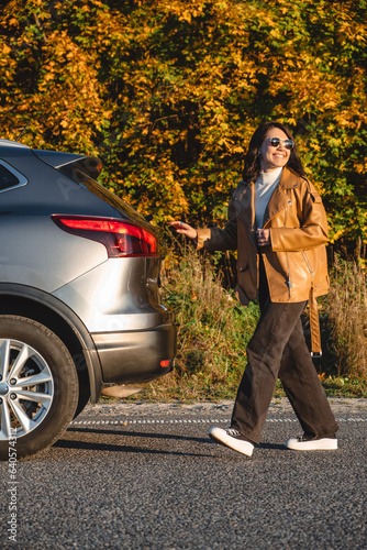 On a forest background, a smiling woman walks next to her car © phpetrunina14