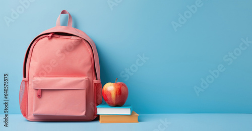Pink school backpack with books and an apple on a blue background