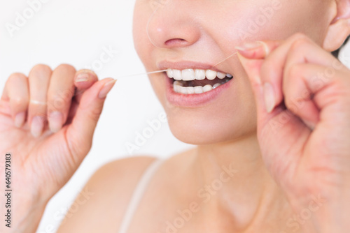 A close-up photo of a young Caucasian woman who uses dental floss to clean her teeth and interdental space. Oral hygiene and maintenance of dental health.