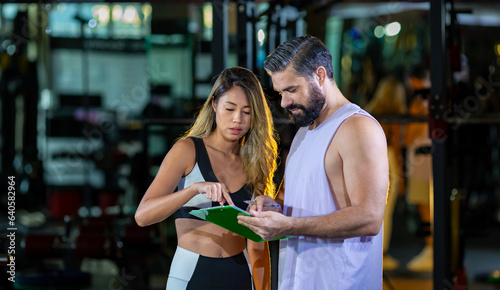 Gym customer is getting advice and suggestion from her personal trainer for exercising plan program and getting her evaluation chart from sample blood test for her workout progress photo