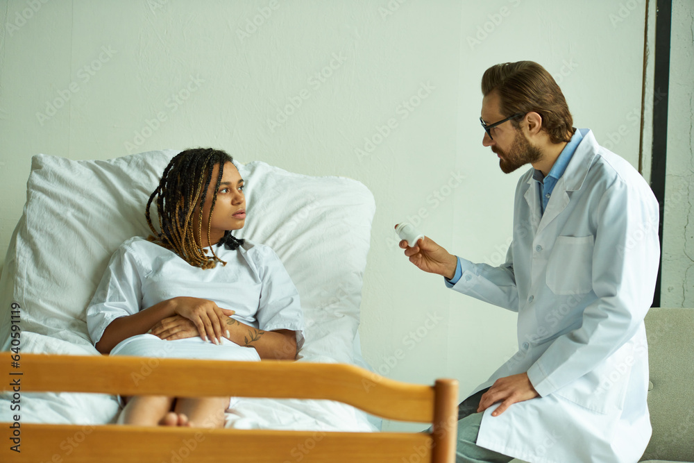 Obraz premium doctor holding bottle with pills near african american woman, private ward, prescribing medication